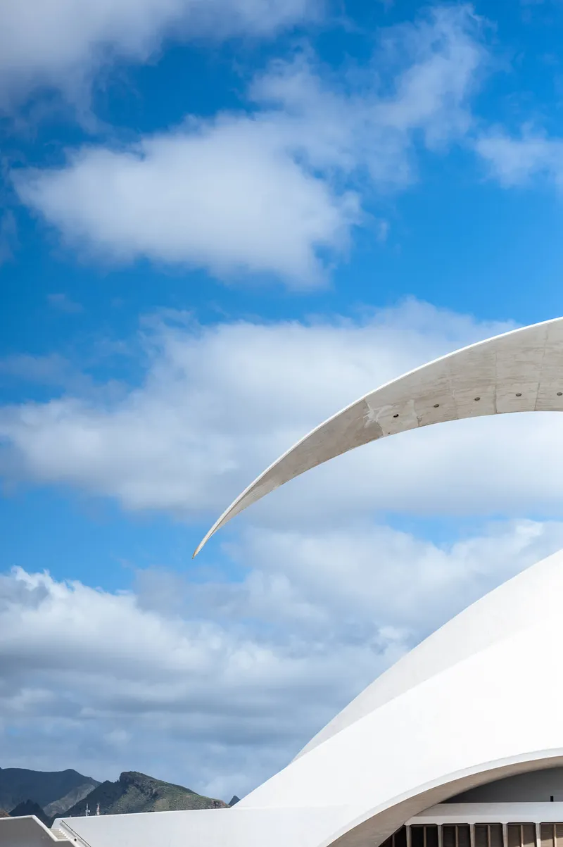 The sweeping arch of the Auditorio de Tenerife against blue sky, the mountains of Tenerife visible in the background