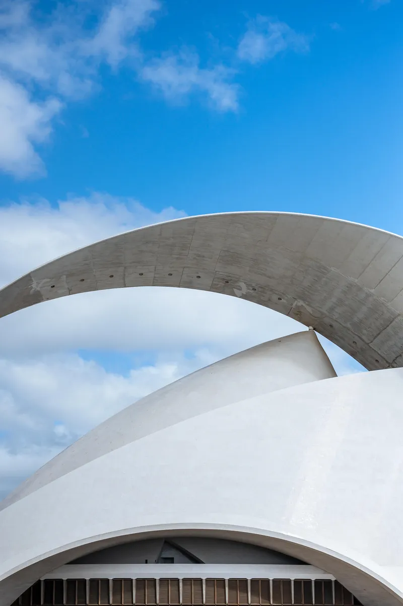 Overlapping concrete arcs of the Auditorio de Tenerife against a blue sky with scattered clouds