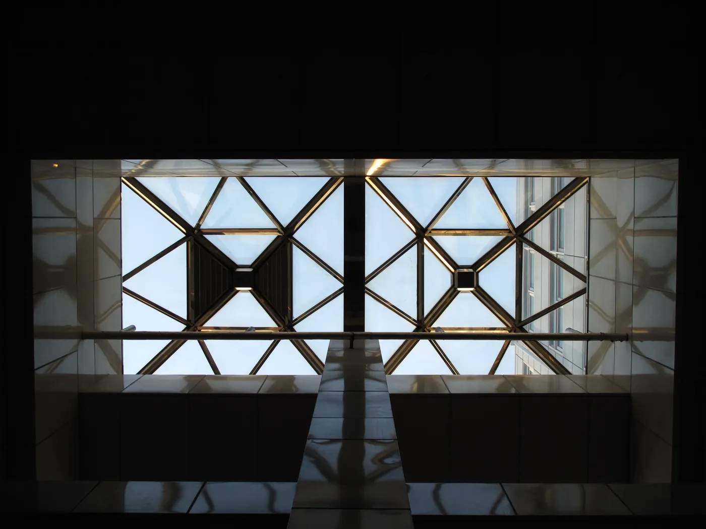 Looking up through two geometric skylight panels in dark steel framing against a bright sky, Japan