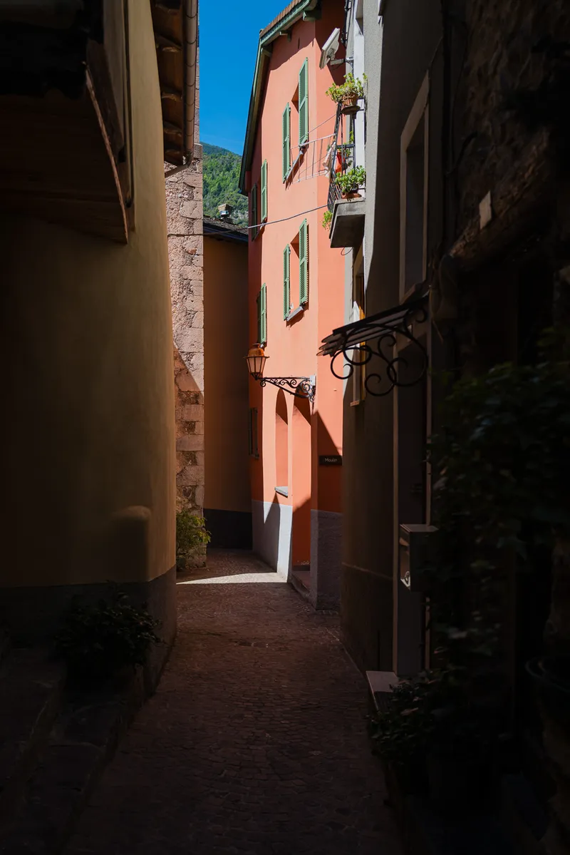 Narrow lane in Saint-Sauveur-sur-Tinée with a coral facade, green shutters, and afternoon light, Alpes-Maritimes, Leica Q2