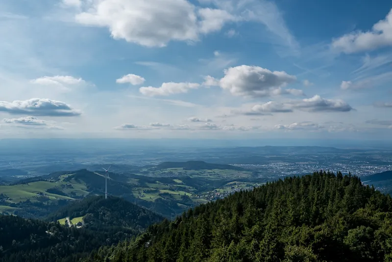 Panoramic view from Schauinsland across the Rhine plain toward Freiburg with layered forested ridges and a wind turbine, Black Forest, Leica Q2