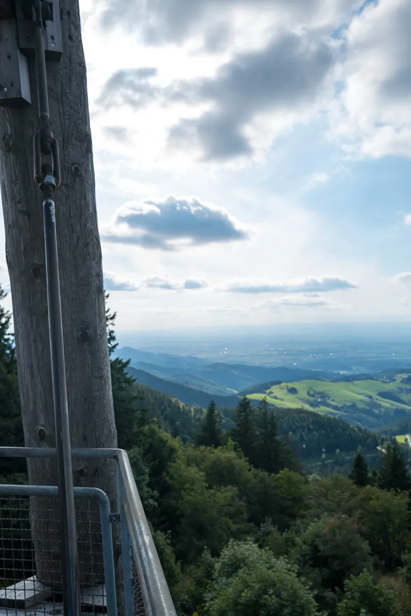 Metal railing and wooden post of the Schauinsland observation tower with Rhine valley and summer sky beyond, Black Forest, Leica Q2