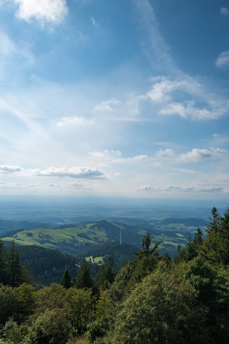 Wide panoramic view from the Schauinsland summit across the Rhine valley, forest, meadows and a wind turbine, Black Forest, Leica Q2