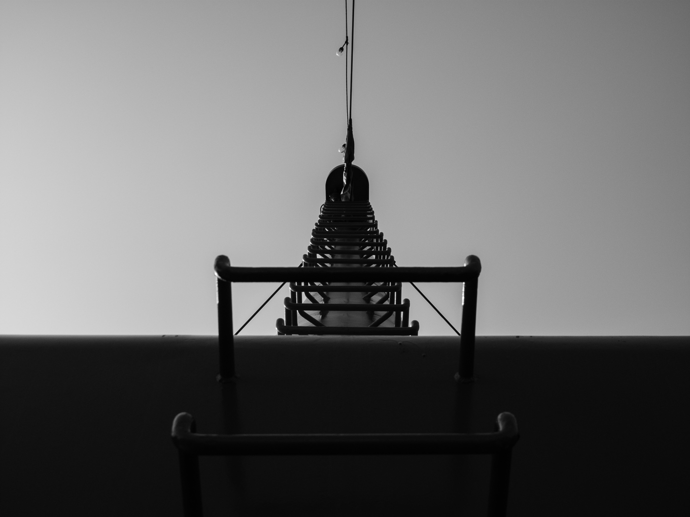 A pagoda spire silhouetted against a flat grey sky, framed by a metal railing, Japan